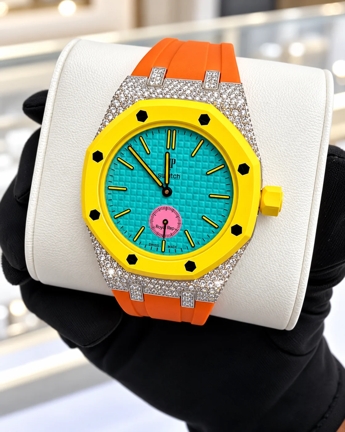 Diamond-set octagonal watch with a yellow bezel, turquoise dial and orange strap, held in a black-gloved hand