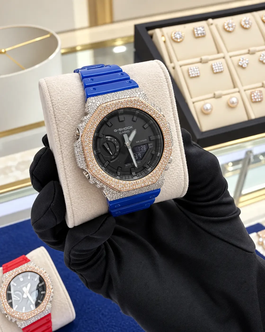 Diamond-set G-Shock with a blue strap held in a black-gloved hand